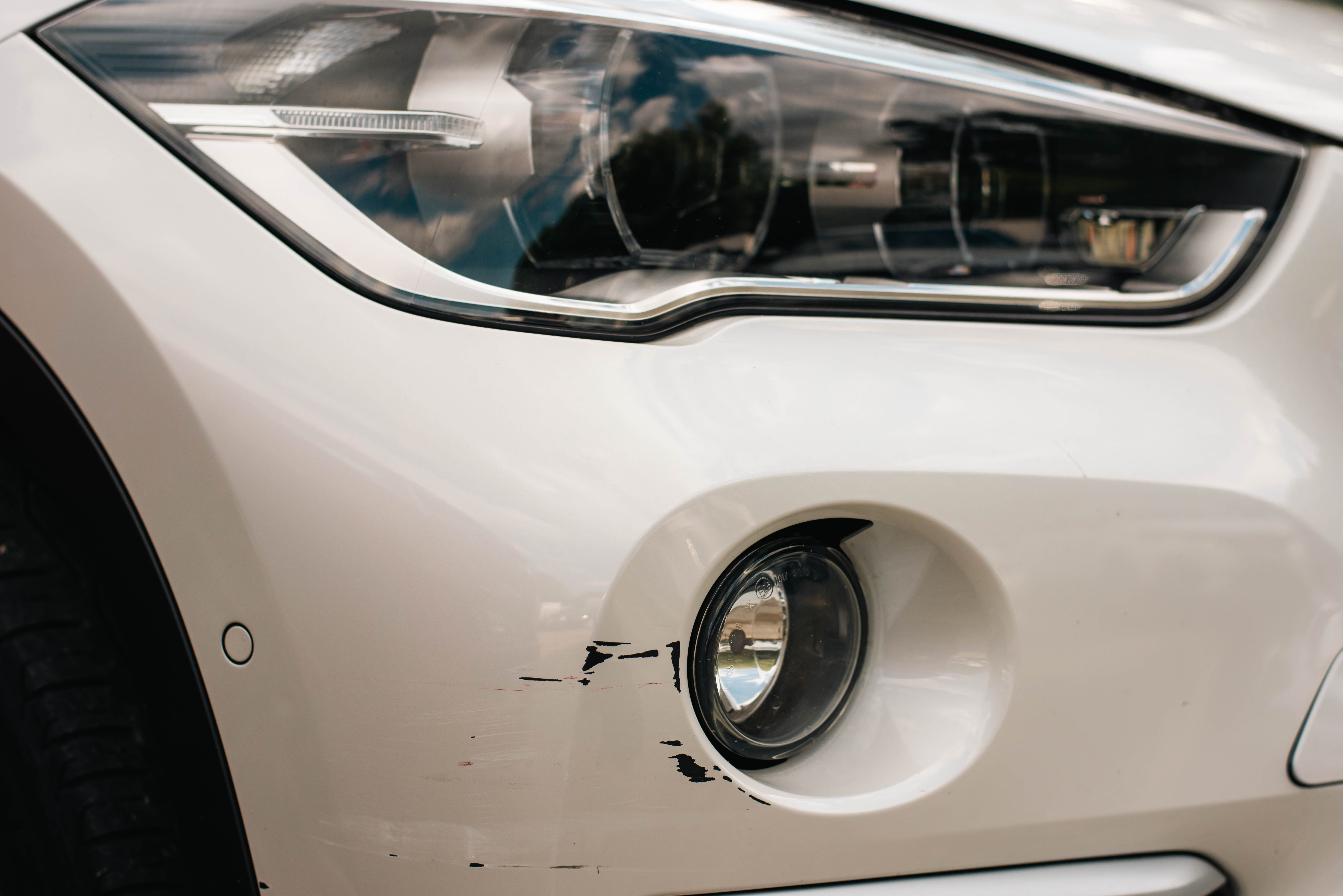 close up of a white car with minor scratch damage around one of the lights